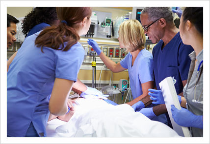 This is a picture of a patient in a er room with six doctor and nurses standing around he patient.